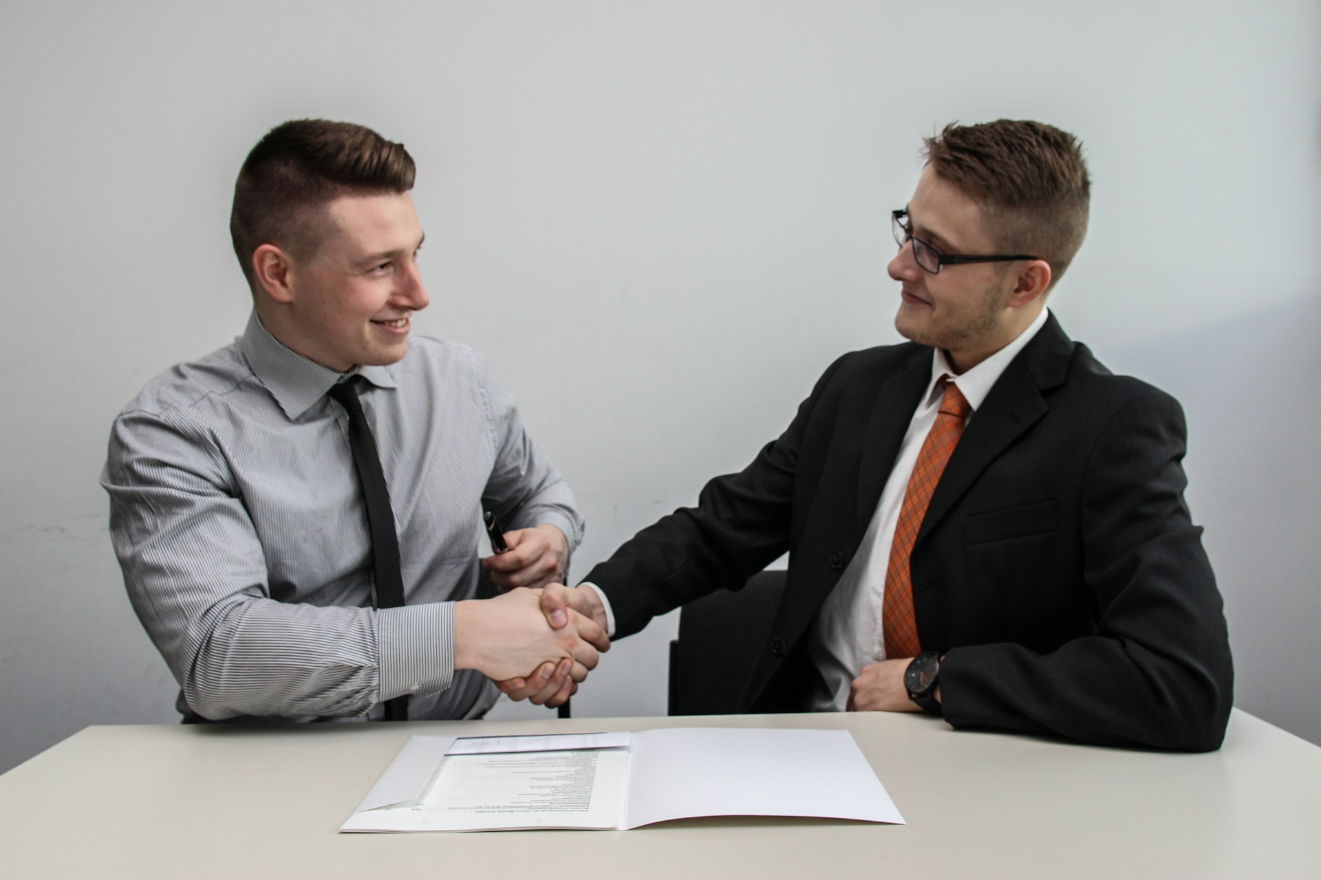 Two men shaking hands at desk with paperwork signifying a deal has been made.