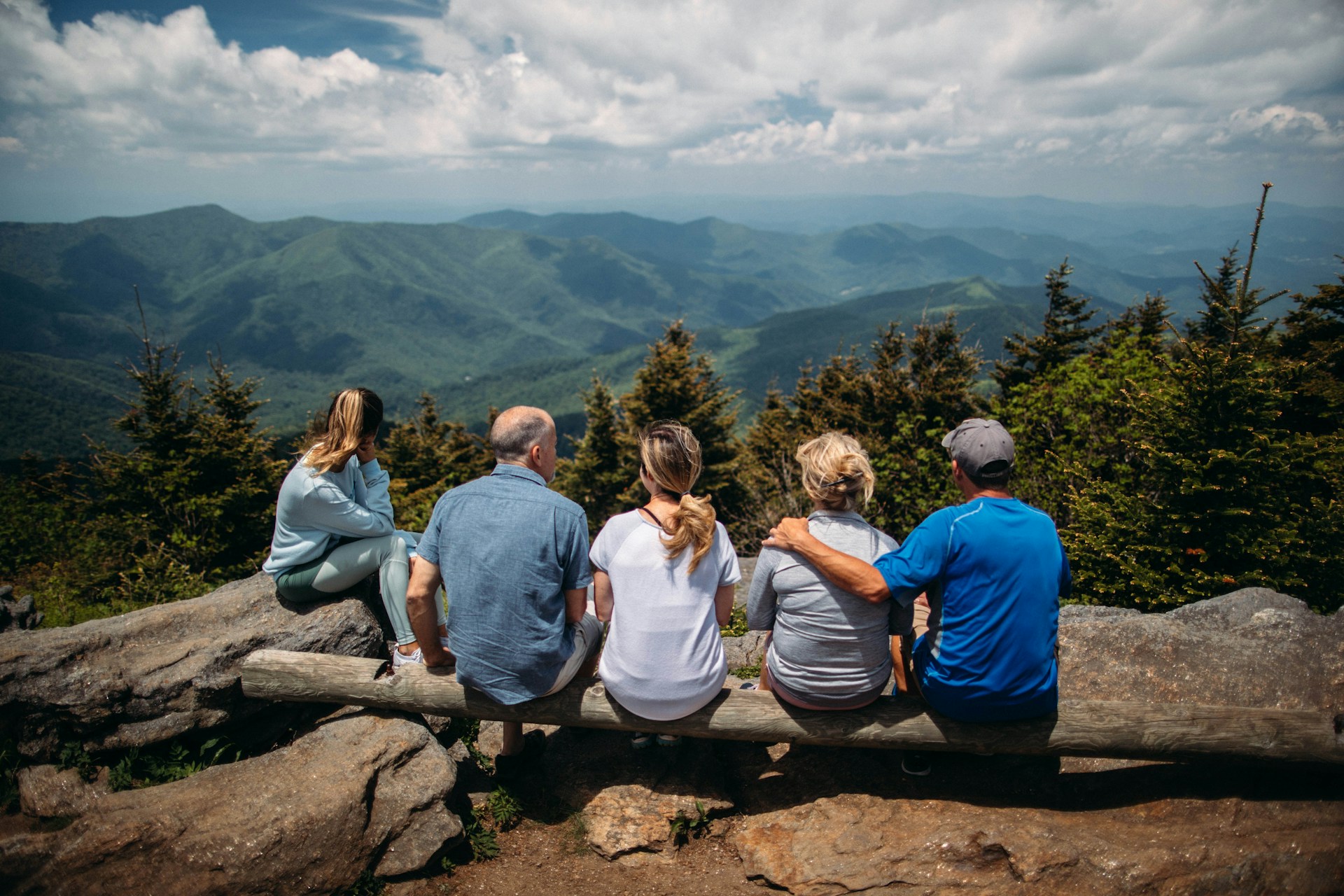 Family generations sitting on a log together on top of a mountain looking out over nature.