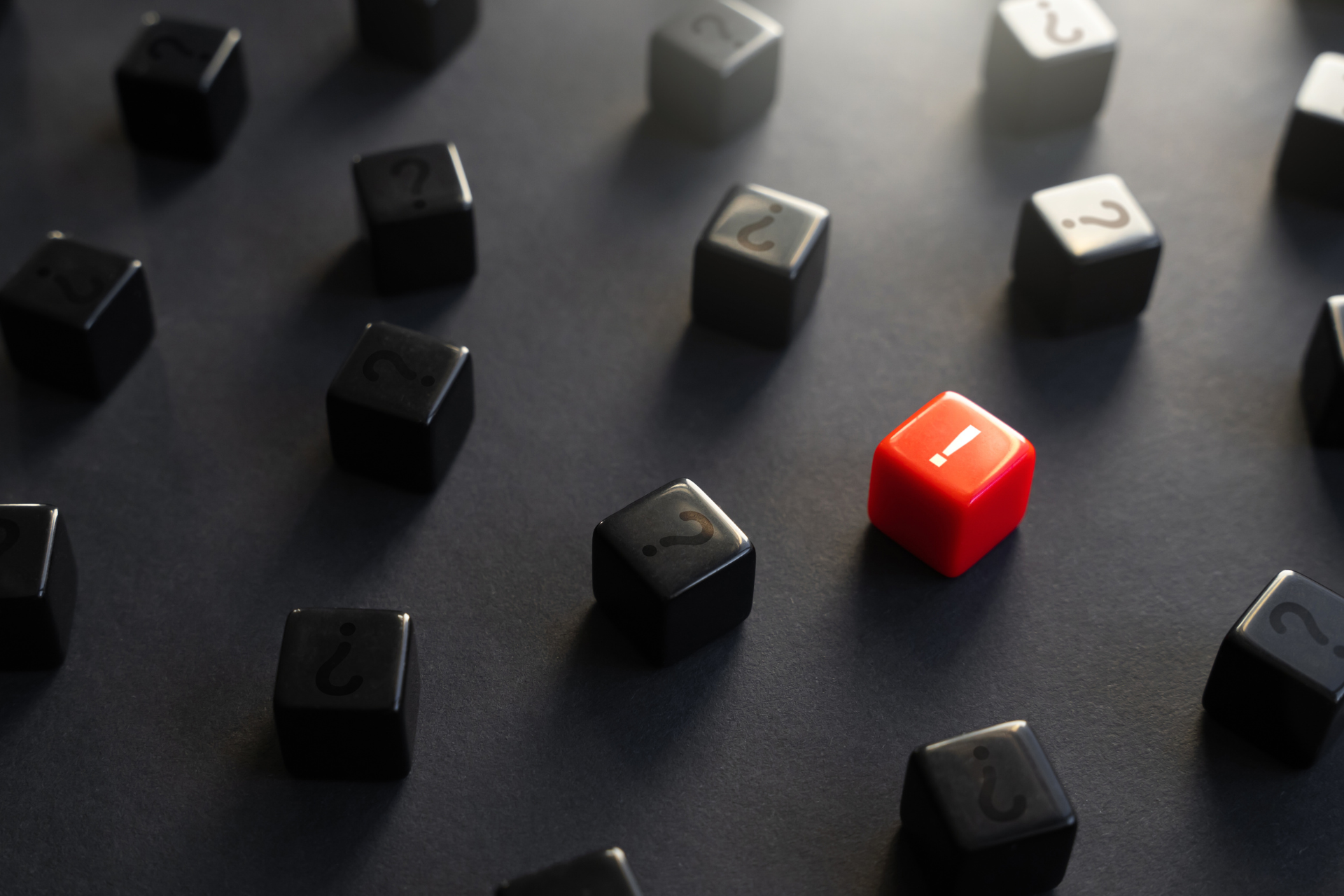 Black dice with question marks and one red die with exclamation point on black background.