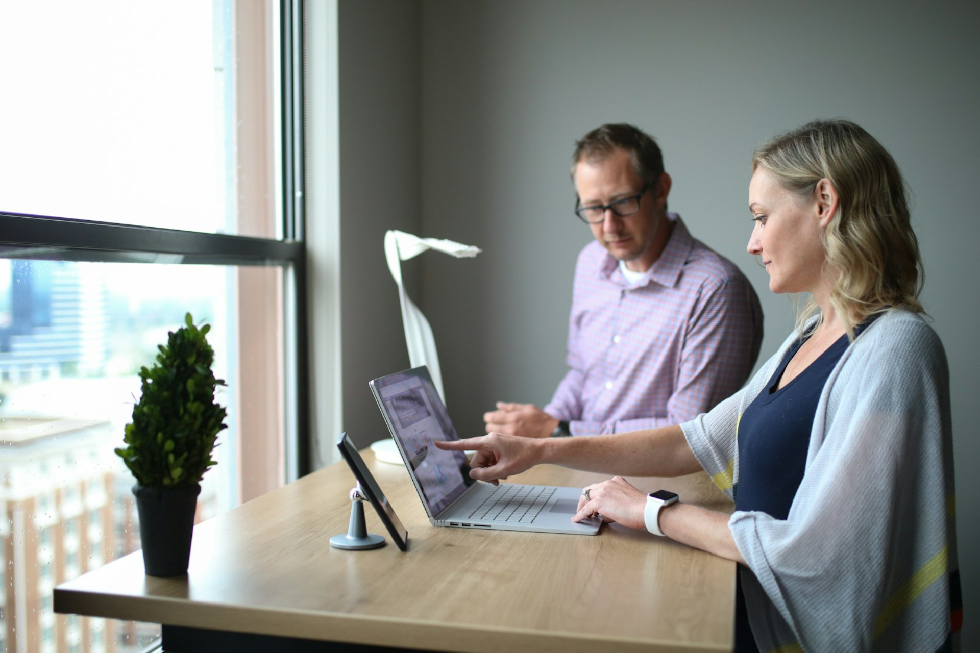 Man and woman standing at a desk review business data on laptop.
